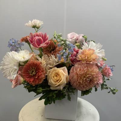 Mixed bouquet of pastel flowers in a white square vase