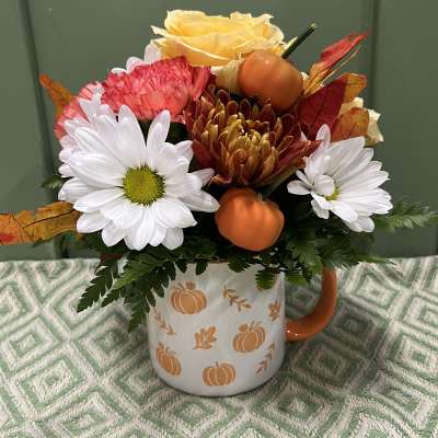 Fall flower arrangement in a pumpkin-decorated mug with daisies and roses
