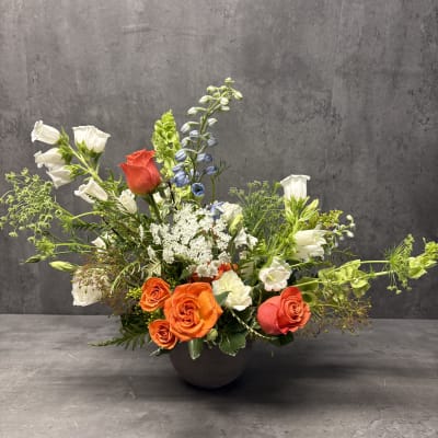 Mixed floral arrangement in a dark bowl vase with orange and white roses