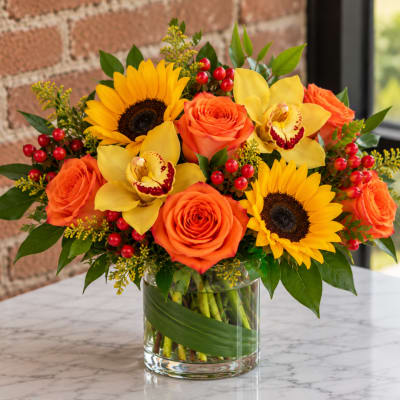 Bouquet of orange roses, sunflowers, and yellow orchids in a glass vase