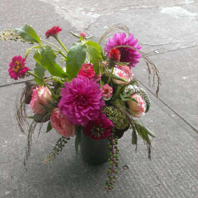 Vase arrangement of bright pink dahlias and blush roses with mixed accents on a concrete surface