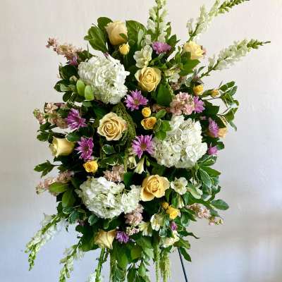 Standing floral spray with yellow roses, white hydrangeas, and purple blooms