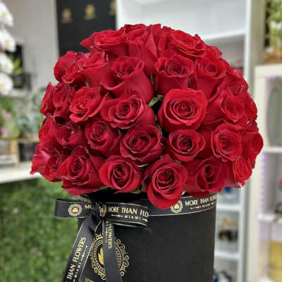 Round black hatbox filled with a dense dome of red roses and tied with a branded black ribbon