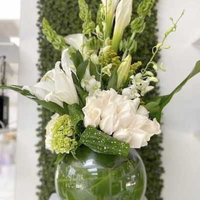 White and green flower arrangement with calla lilies and roses in a round glass vase