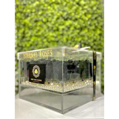 Clear acrylic box of black preserved roses with pearl accents against a green wall