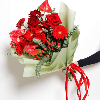 Bouquet of red roses and gerbera daisies wrapped in pale green paper