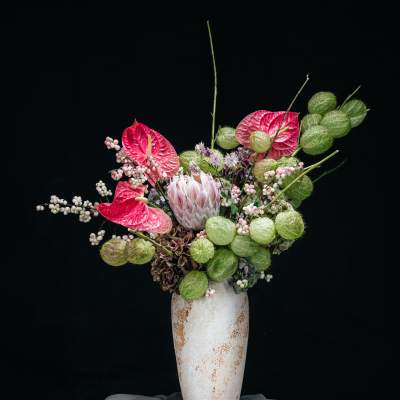 Pink anthuriums and pale flowers in a tall white vase
