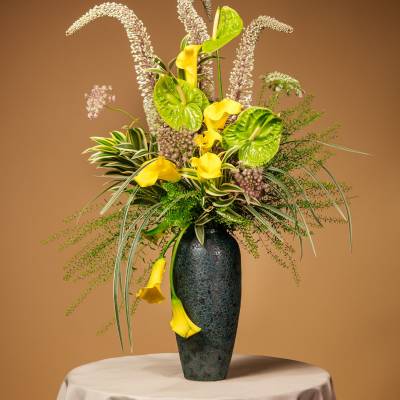 Tall floral arrangement with yellow calla lilies in a dark vase