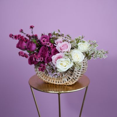 Pink and white roses in a woven basket on a small stand