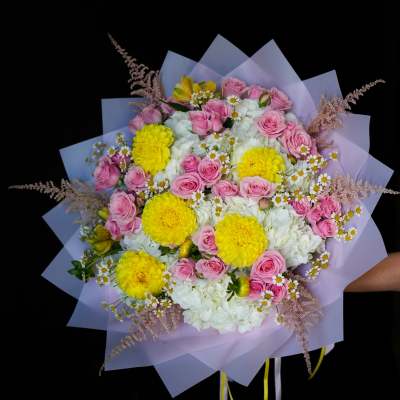 Bouquet of pink roses, yellow blooms, and white flowers wrapped in lavender paper
