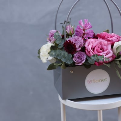 Pink and purple flowers arranged in a gray gift box with handles