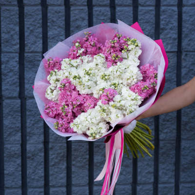 Pink and white flower bouquet wrapped in tissue paper with ribbon tails