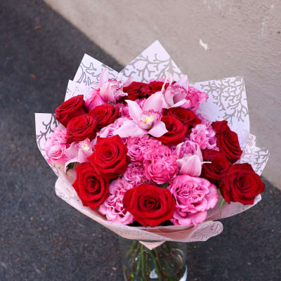 Bouquet of red and pink roses with pale pink orchids in a glass vase