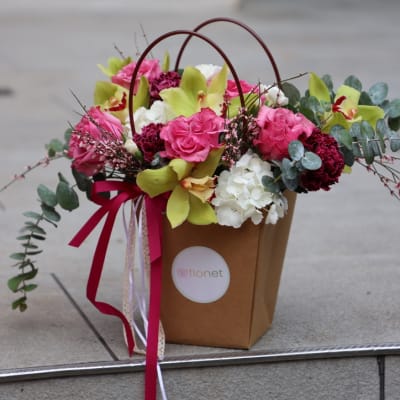 Pink and white flower arrangement in a brown gift bag with ribbon handles