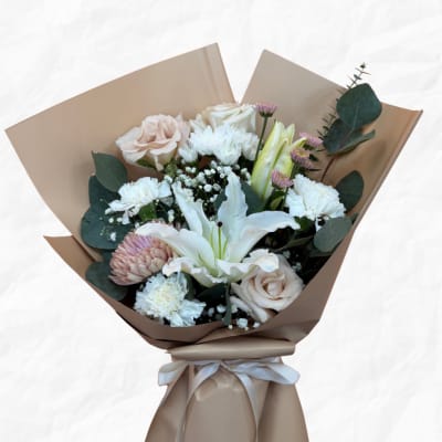 Bouquet of pale roses, white lilies, and chrysanthemums wrapped in tan paper