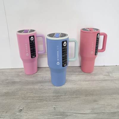 Set of three tall handled travel tumblers in pastel pink, blue, and coral on a wood floor