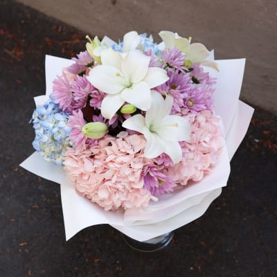Bouquet of white lilies, pink chrysanthemums, and blue hydrangeas in white wrap