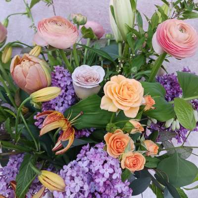 Garden-style arrangement with peach roses, pink ranunculus, lilies, and purple lilacs