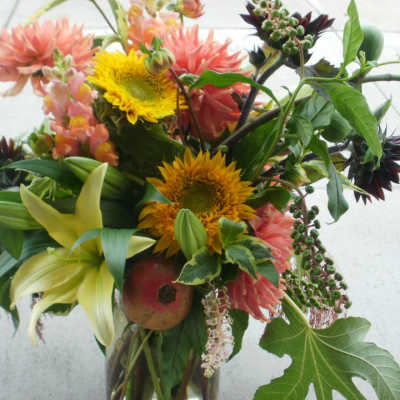 Loose garden-style bouquet with yellow sunflowers, peach dahlias, and lilies in a clear glass vase