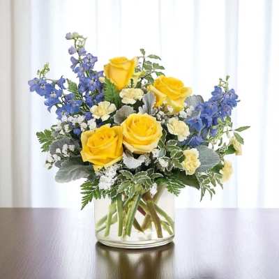 Yellow roses and blue delphinium in a clear glass vase