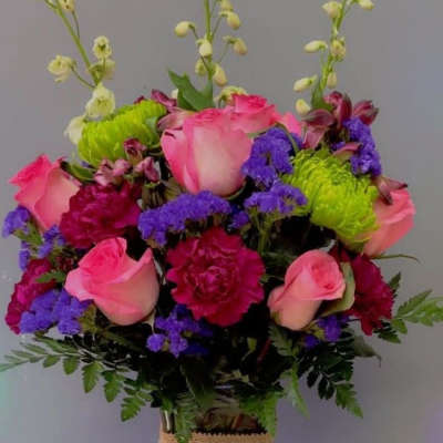 Pink roses and purple flowers arranged in a glass vase with burlap wrap