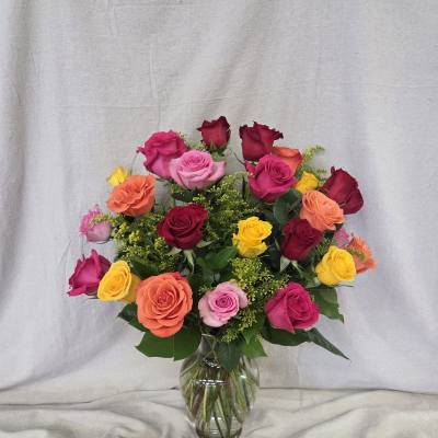 Mixed bouquet of bright roses in pink, orange, yellow, and red arranged in a clear glass vase