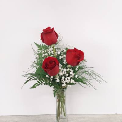 Tall clear vase with three red roses and small white accent flowers.