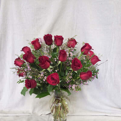 Tall arrangement of red roses with tiny pink blooms in a clear glass vase