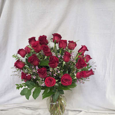 Tall arrangement of long-stem red roses with small pink filler flowers in a clear glass vase