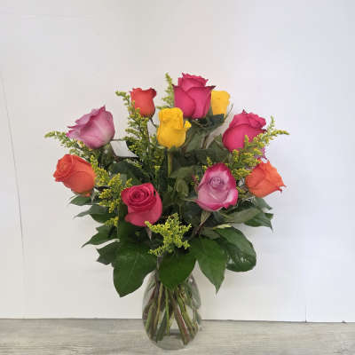 Glass vase of mixed pink, yellow, orange, and lavender roses with yellow filler flowers