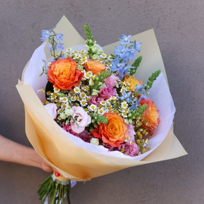 Hand-tied bouquet of orange roses, blue flowers, and small white daisies