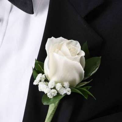 White rose boutonniere with small white filler flowers pinned to a black suit lapel