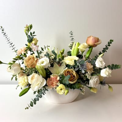 Mixed bouquet of roses, lilies, and carnations in a white bowl vase
