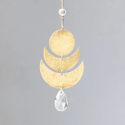 Gold hanging ornament with circular and crescent shapes and a clear teardrop crystal