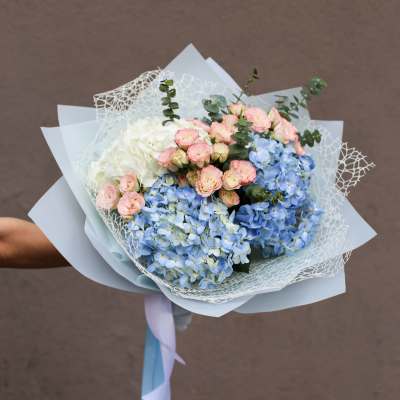 Hand-tied bouquet of blue hydrangeas, pink spray roses, and white blooms
