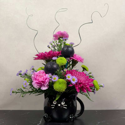 Pink and purple flower arrangement in a black cat mug with curly wire accents