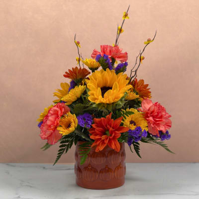 Colorful bouquet of sunflowers, carnations, and purple filler in an amber vase