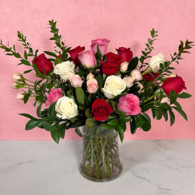 Mixed roses in a clear glass vase against a pink background