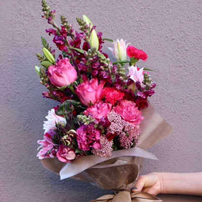 Hand-tied bouquet of pink and magenta flowers wrapped in brown paper