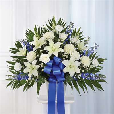 White lilies and chrysanthemums with blue flowers and a blue ribbon in a vase