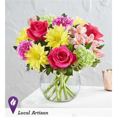 Mixed bouquet of pink roses, yellow daisies, and pastel flowers in a clear glass vase