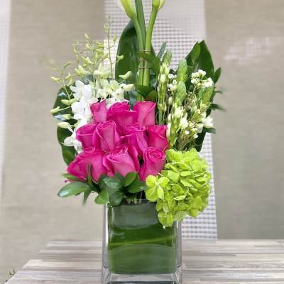 Tall modern arrangement with white calla lilies, hot pink roses, and green hydrangea in a glass cube vase