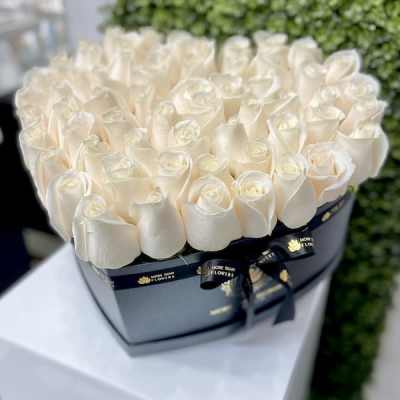 Heart-shaped black box filled with tightly packed ivory roses on a white pedestal