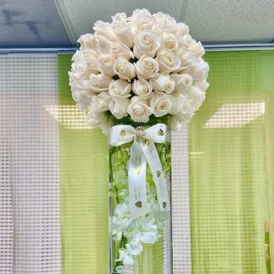 Tall glass cylinder vase with submerged white orchids topped by a dense dome of ivory roses and ribbon.