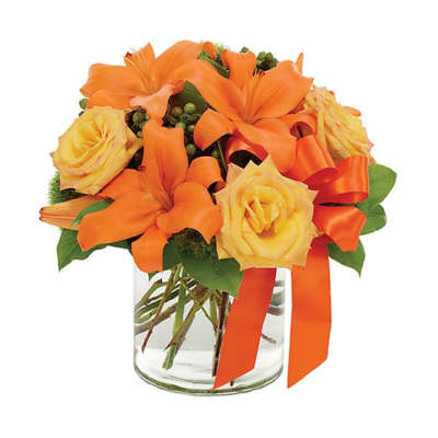 Orange lilies and yellow roses in a clear glass vase with an orange ribbon