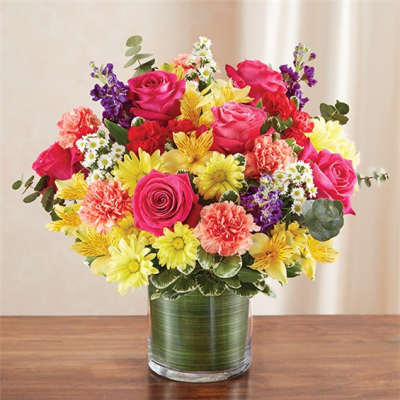 Mixed bouquet of pink roses, yellow daisies, and carnations in a glass vase