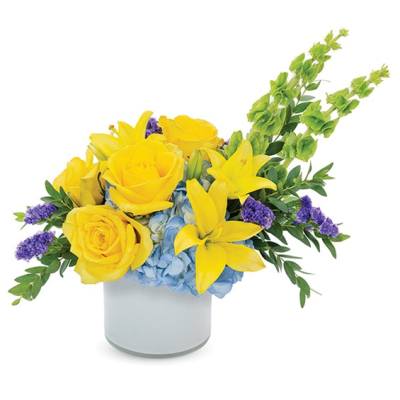 Yellow roses and lilies in a white vase with blue hydrangeas