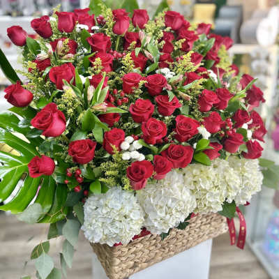 Large basket arrangement of red roses and white hydrangeas with bold green leaves
