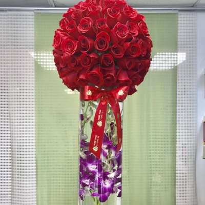 Tall glass vase with submerged purple orchids topped by a large red rose sphere and red ribbon