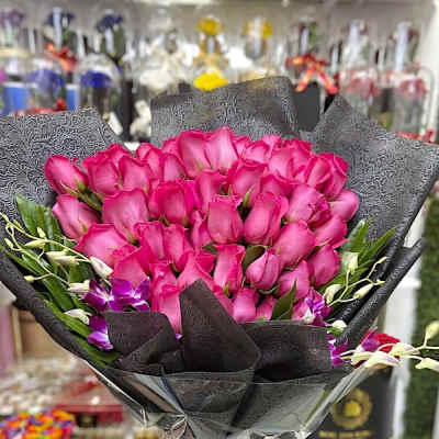 Large bouquet of bright pink roses with purple orchids wrapped in black paper.